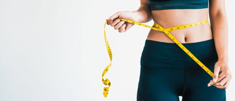 A woman in athletic wear measuring her waist with a yellow tape measure, symbolizing progress and success in losing weight on semaglutide.